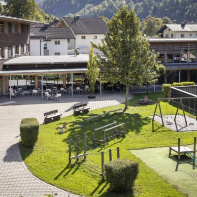 Sie sehen den Blick in den Innenhof des JUFA Hotels Montafon*** mit Spielewiese und Schaukel. Das JUFA Hotel Montafon*** steht für Familienurlaub und unvergessliche Winter- und Wanderurlaube.